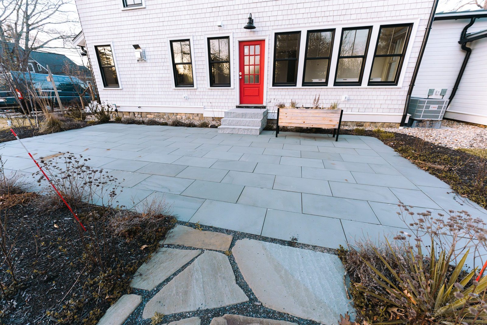A bluestone and flagstone terrace beside a white house, with planted beds along the edge.