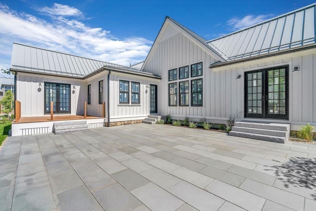 A white modern farmhouse with a large paver terrace under a clear sky.